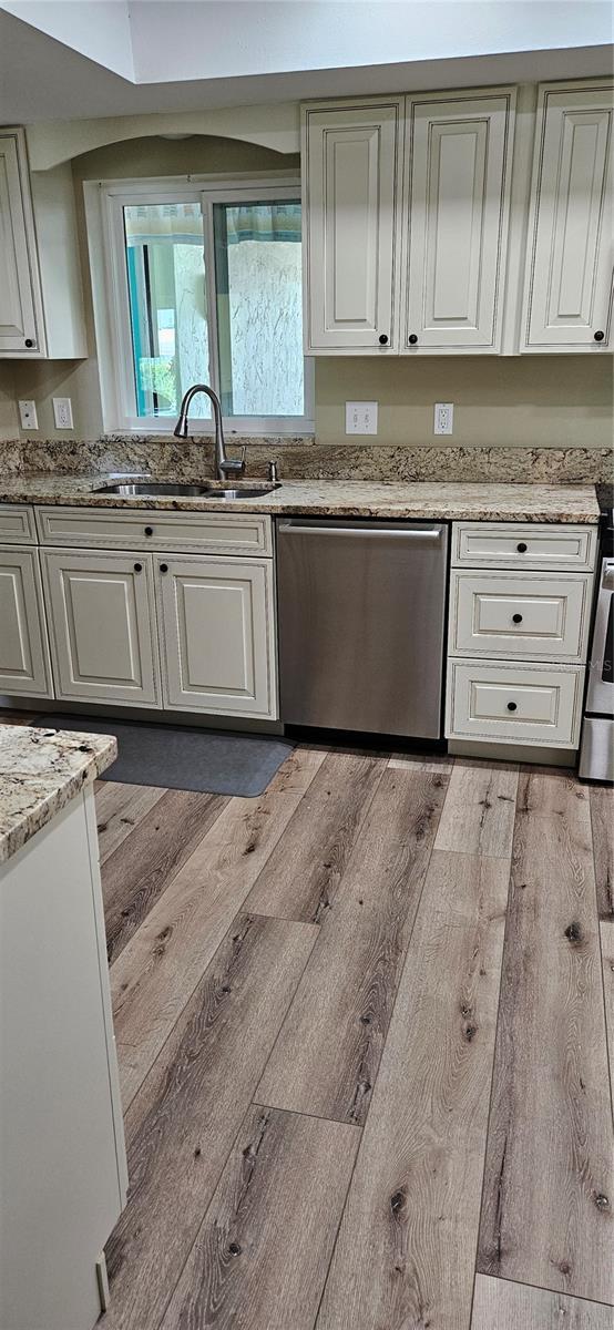 kitchen with white cabinetry, light wood finished floors, a sink, and dishwasher