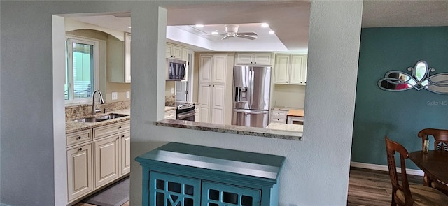 kitchen featuring a sink, a tray ceiling, stainless steel appliances, dark wood-type flooring, and light stone countertops