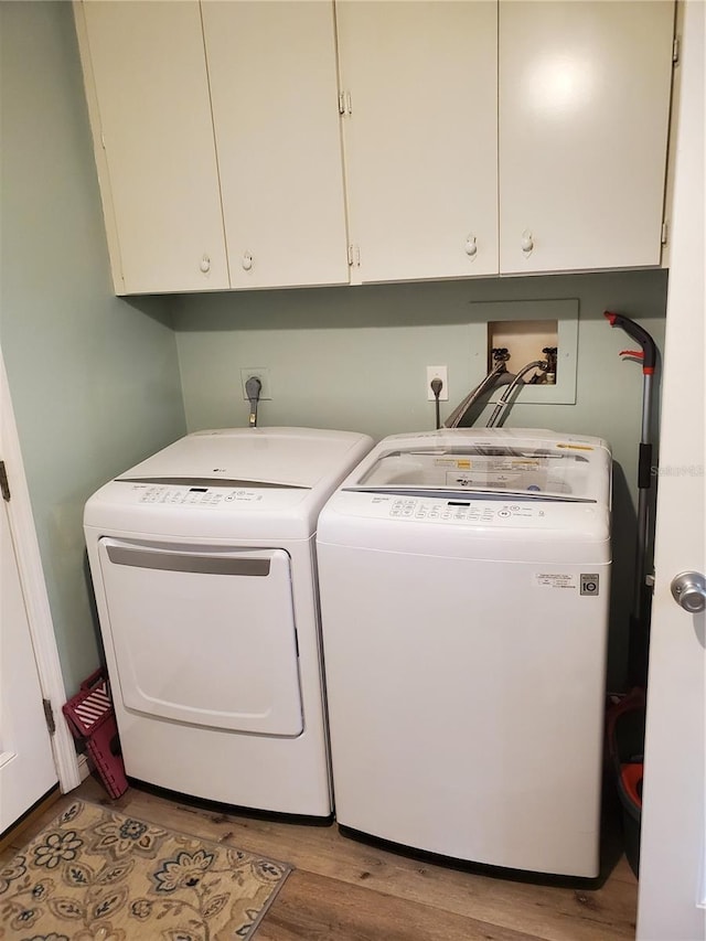 clothes washing area with washer and dryer, cabinet space, and wood finished floors