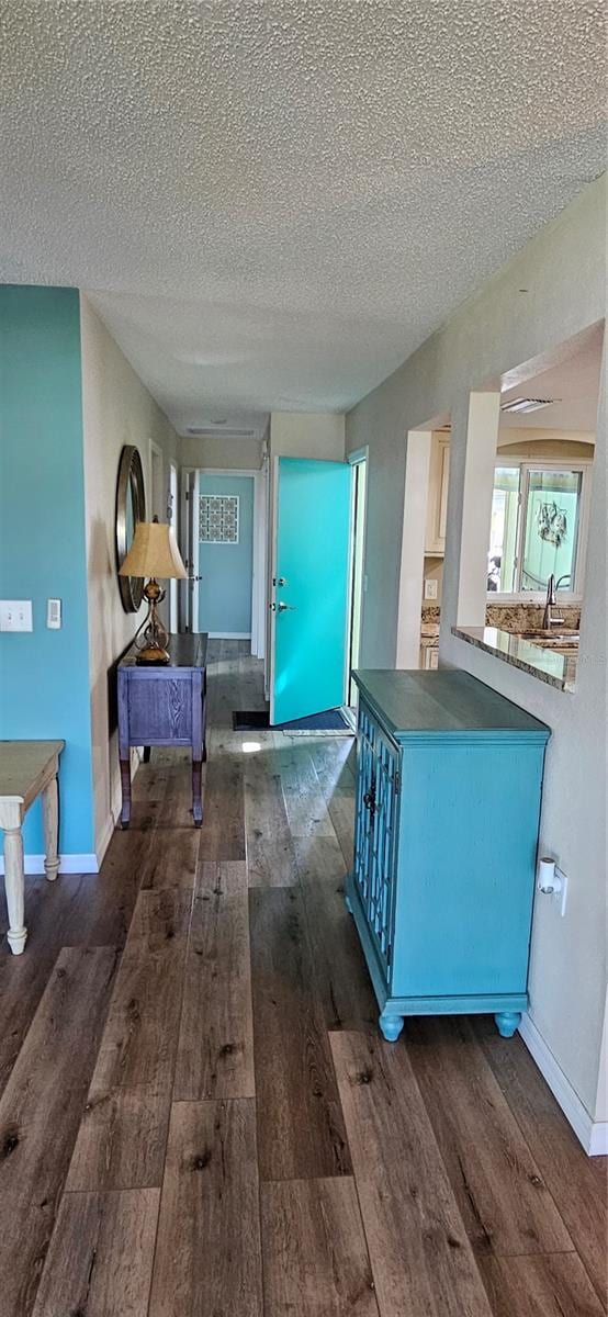 hall with baseboards, a textured ceiling, and dark wood-type flooring