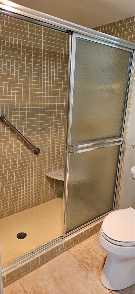 bathroom featuring a shower stall, tile patterned floors, and toilet