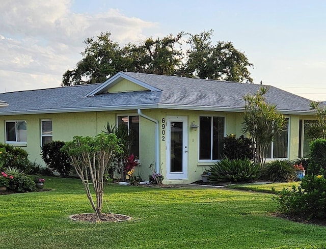 ranch-style home with a front lawn, stucco siding, and roof with shingles