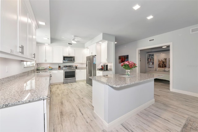 kitchen with a ceiling fan, a sink, light wood finished floors, stainless steel appliances, and white cabinetry