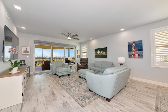 living area with light wood-style floors, baseboards, plenty of natural light, and a ceiling fan