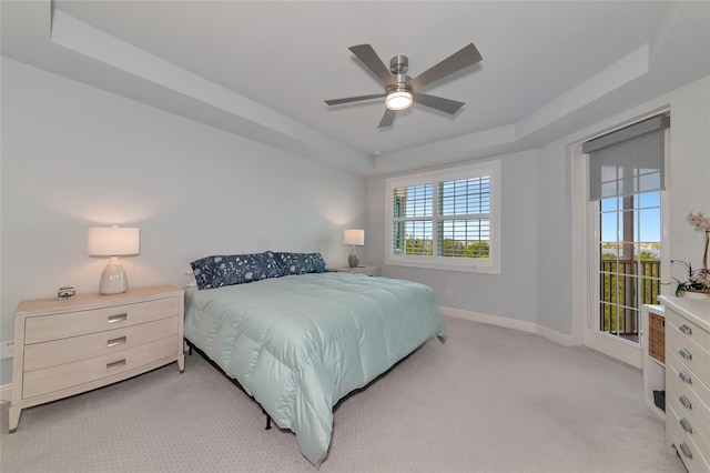 bedroom featuring a tray ceiling, ceiling fan, light carpet, and baseboards