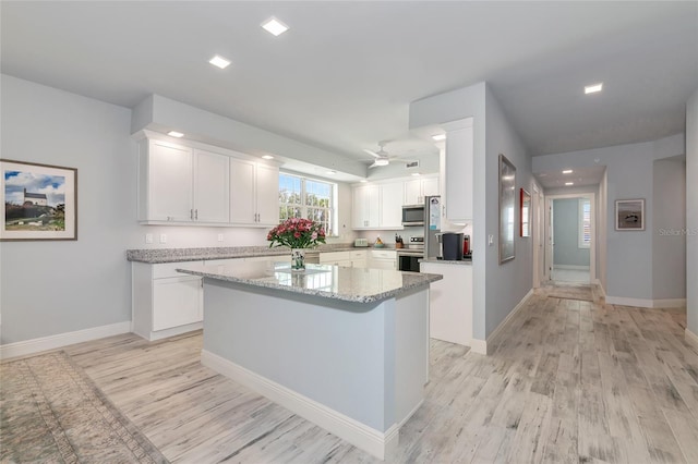 kitchen featuring white cabinets, light stone countertops, stainless steel appliances, light wood-type flooring, and a kitchen island