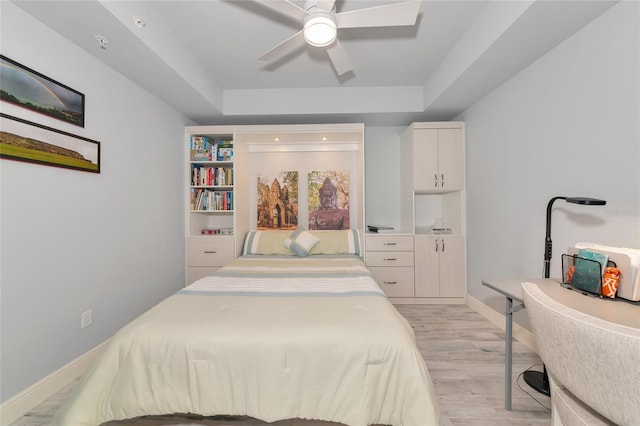 bedroom featuring baseboards, light wood finished floors, ceiling fan, and a tray ceiling