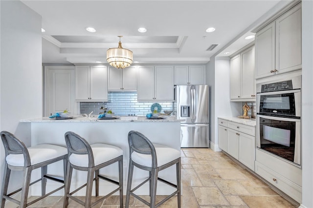 130 Riviera Dunes Way Unit 502, Palmetto, FL 34221 - kitchen featuring appliances with stainless steel finishes, a breakfast bar, tasteful backsplash, a tray ceiling, and visible vents