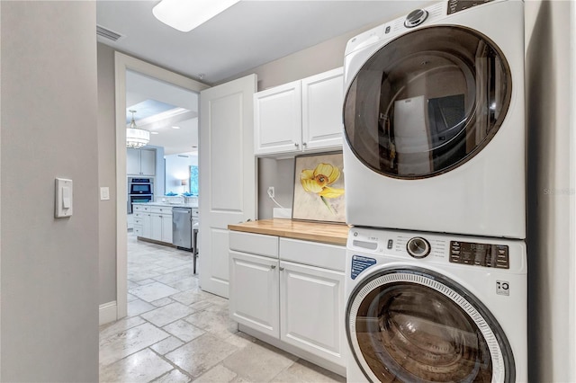 130 Riviera Dunes Way Unit 502, Palmetto, FL 34221 - laundry room with cabinet space, stacked washer and dryer, stone tile floors, baseboards, and visible vents