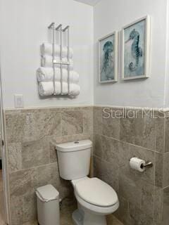 bathroom featuring tile walls, wainscoting, and toilet