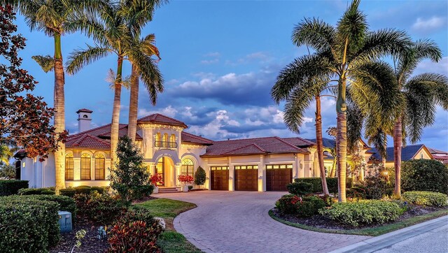 mediterranean / spanish house with stucco siding, decorative driveway, a tile roof, and a garage