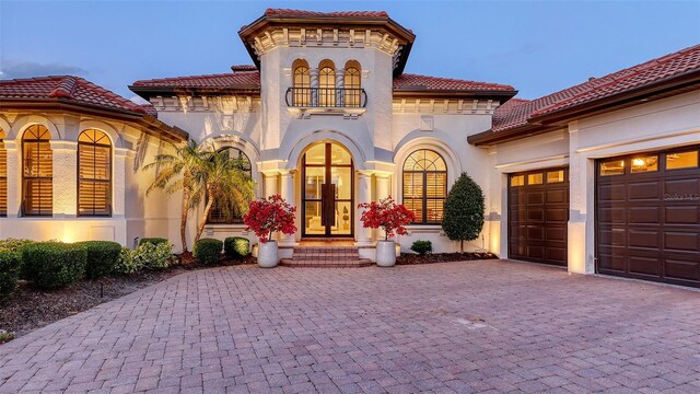 mediterranean / spanish-style house with a garage, stucco siding, decorative driveway, a balcony, and a tiled roof