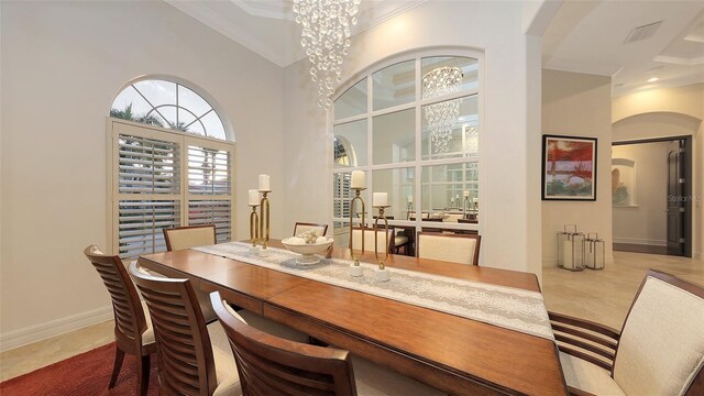 tiled dining area featuring visible vents, ornamental molding, a towering ceiling, baseboards, and arched walkways