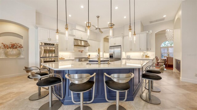 kitchen with appliances with stainless steel finishes, a sink, arched walkways, baseboards, and under cabinet range hood