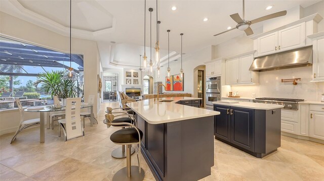 kitchen featuring appliances with stainless steel finishes, arched walkways, a large island with sink, a sink, and under cabinet range hood