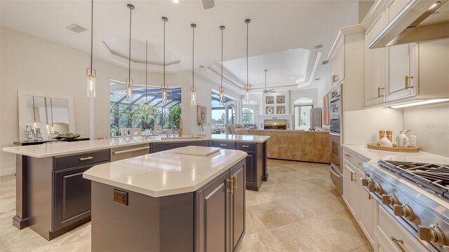kitchen with a tray ceiling, a kitchen island with sink, visible vents, open floor plan, and under cabinet range hood