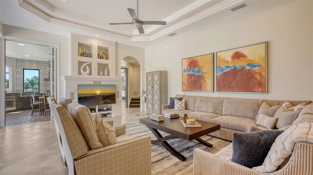 living room with visible vents, built in features, ceiling fan, a tray ceiling, and arched walkways