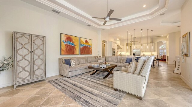 living room featuring arched walkways, ceiling fan, baseboards, and a raised ceiling
