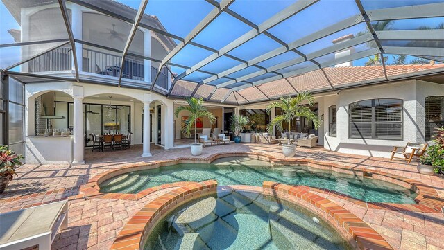 rear view of property with a balcony, outdoor dining area, a patio area, a lanai, and a pool with connected hot tub
