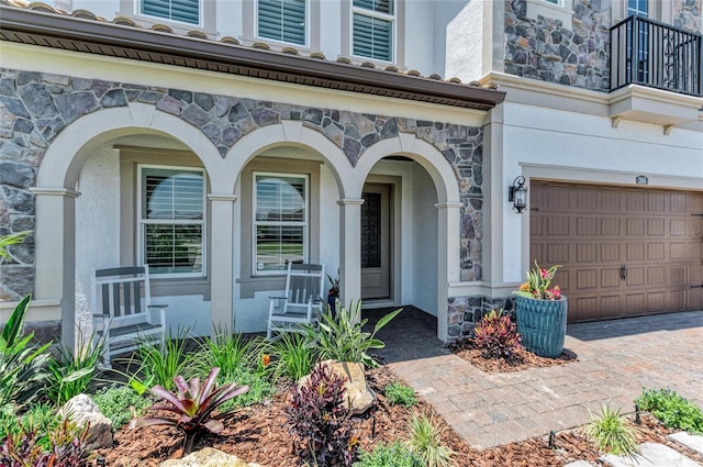 entrance to property with a garage, a balcony, stone siding, and stucco siding