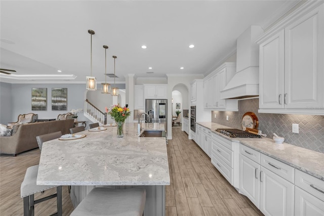 kitchen featuring custom exhaust hood, open floor plan, a kitchen breakfast bar, appliances with stainless steel finishes, and backsplash