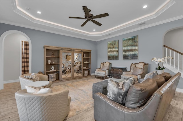 living area featuring ceiling fan, visible vents, arched walkways, a tray ceiling, and stairs