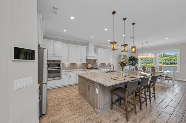 kitchen with decorative backsplash, a breakfast bar area, a sink, premium range hood, and white cabinetry