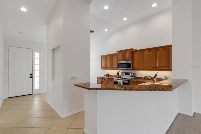 kitchen featuring stainless steel appliances, dark stone counters, brown cabinets, baseboards, and recessed lighting