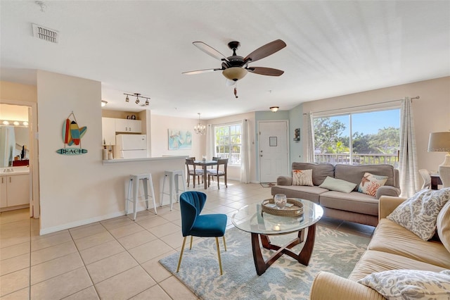 living room with light tile patterned floors, visible vents, baseboards, and ceiling fan with notable chandelier