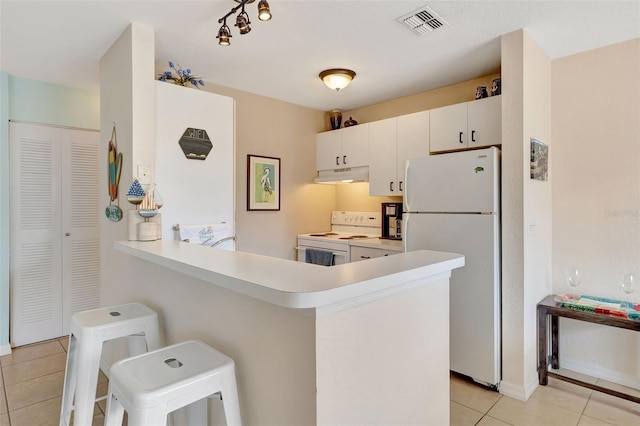kitchen featuring a peninsula, light tile patterned floors, white appliances, under cabinet range hood, and light countertops