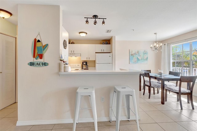 kitchen with a peninsula, light tile patterned floors, a breakfast bar area, white appliances, and a chandelier