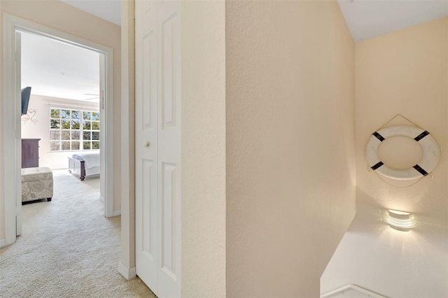 hallway featuring light colored carpet and baseboards