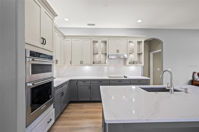 9106 Yarberry St, Sarasota, FL 34240 - kitchen with gray cabinetry, under cabinet range hood, a sink, arched walkways, and double oven