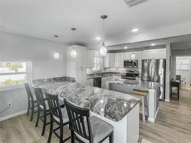 kitchen with a kitchen breakfast bar, dark stone countertops, a sink, appliances with stainless steel finishes, and baseboards