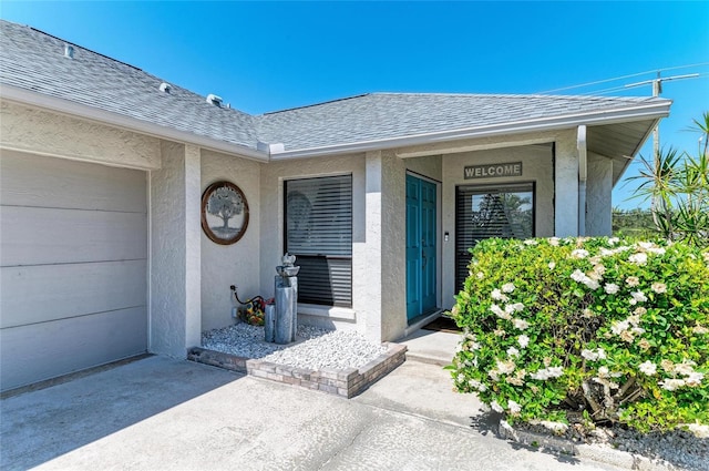 entrance to property featuring an attached garage, a shingled roof, stucco siding, and concrete driveway