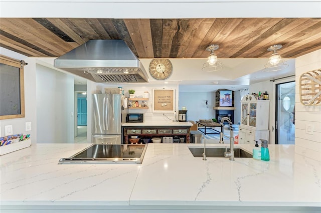kitchen featuring freestanding refrigerator, wood ceiling, stovetop, and wall chimney range hood