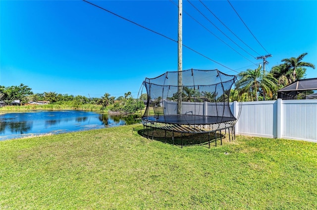 view of yard with fence, a trampoline, and a water view