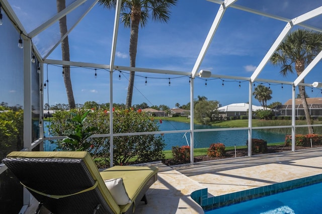 outdoor pool with glass enclosure, a water view, and a patio