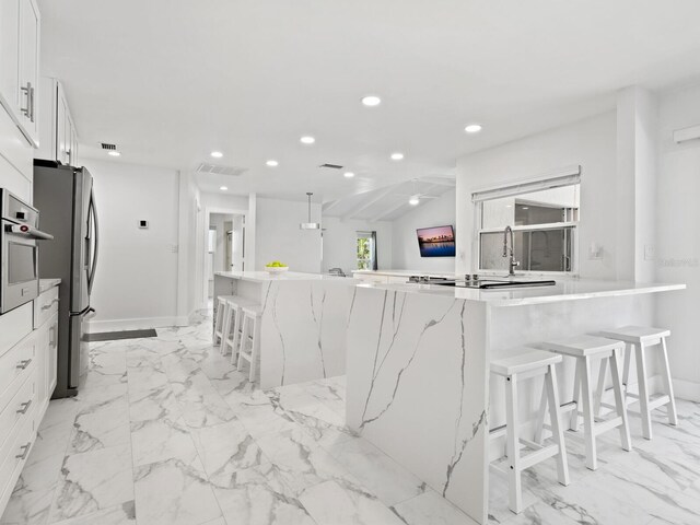 172 Sea Anchor Dr, Osprey, FL 34229 - kitchen with white cabinetry, recessed lighting, stainless steel appliances, a breakfast bar, and light marble finish floors