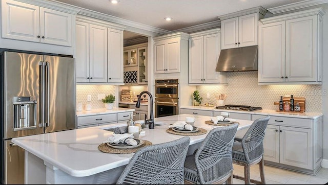 kitchen featuring a breakfast bar area, under cabinet range hood, appliances with stainless steel finishes, light countertops, and a sink