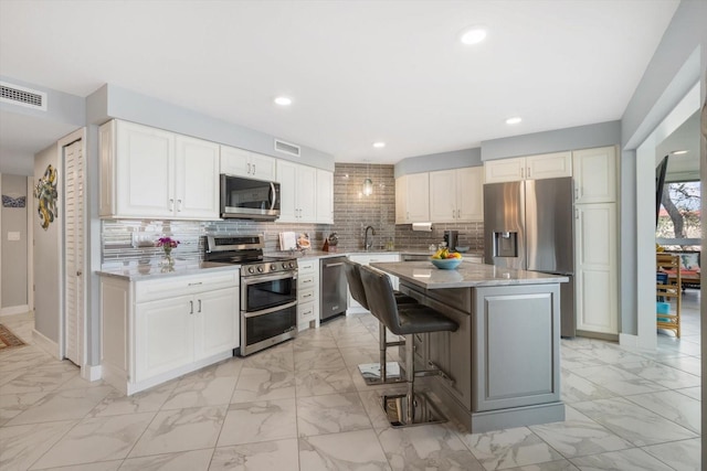 kitchen with a kitchen island, visible vents, appliances with stainless steel finishes, marble finish floor, and a breakfast bar