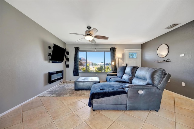 living area featuring light tile patterned flooring, visible vents, a ceiling fan, and baseboards