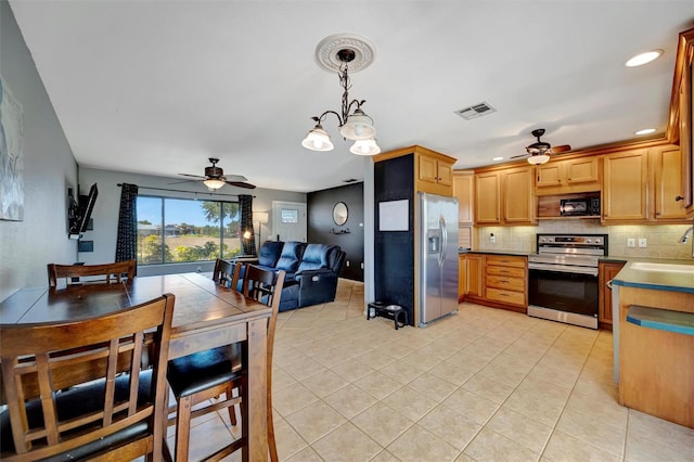 kitchen with tasteful backsplash, ceiling fan with notable chandelier, appliances with stainless steel finishes, and a sink