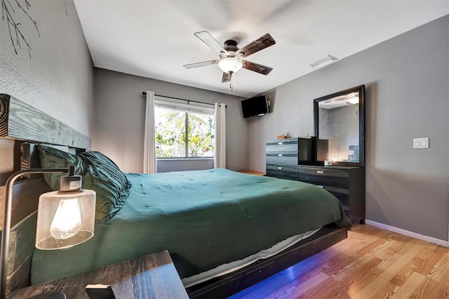 bedroom featuring a ceiling fan, visible vents, wood finished floors, and baseboards