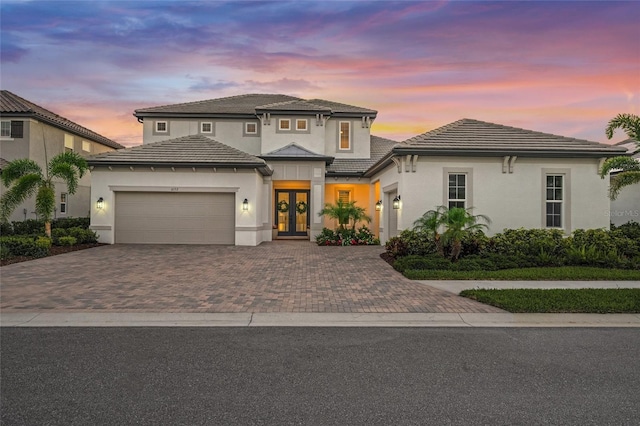 view of front facade featuring french doors, an attached garage, stucco siding, and decorative driveway