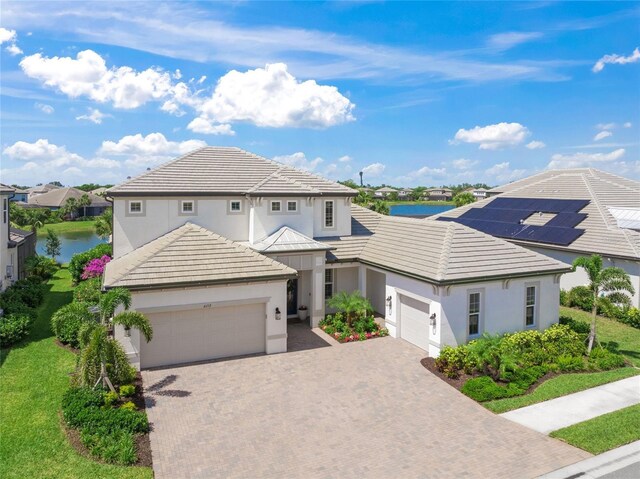 traditional home featuring a water view, an attached garage, decorative driveway, and stucco siding