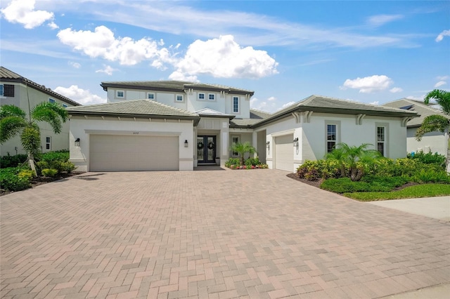 prairie-style house with french doors, stucco siding, decorative driveway, and a garage