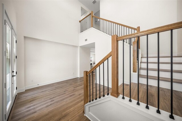 staircase with baseboards, wood finished floors, and a towering ceiling