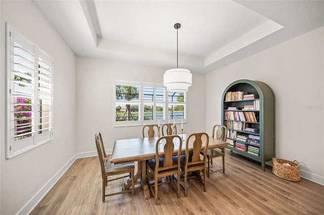 dining area with light wood-type flooring, a raised ceiling, and baseboards