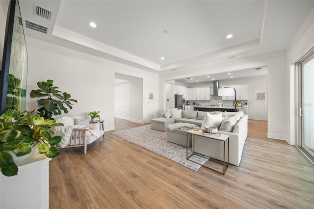 living room featuring visible vents, baseboards, recessed lighting, a tray ceiling, and light wood finished floors